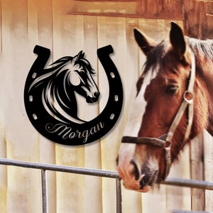 May include: Black metal horseshoe with a horse head silhouette inside and the name "Morgan" written below. The horseshoe is mounted on a wooden wall.