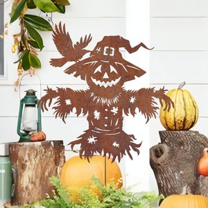 May include: A rusty metal Halloween scarecrow with a pumpkin face and a crow perched on its hat. The scarecrow is standing in front of a white wooden wall with pumpkins on the ground.
