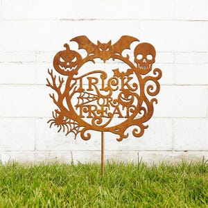 May include: A rusty brown metal Halloween garden stake with a circular design. The design includes a jack-o'-lantern, bat, skull, spider, and the words "Trick or Treat". The stake is in a grassy yard.