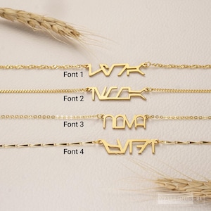 Könnte beinhalten: Vier goldfarbene Halsketten mit dem Namen Nova in verschiedenen typografischen Stilen. Jede Halskette ist mit Text beschriftet, der Font 1, Font 2, Font 3 und Font 4 angibt, und zeigt Variationen in der Buchstabenstruktur und den Kettengliedern.
