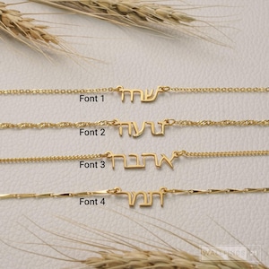 May include: Four gold-toned necklaces featuring Hebrew name pendants in distinct styles, labeled Font 1, Font 2, Font 3, and Font 4. Each necklace consists of a delicate metal chain connected to a custom script nameplate, showcasing varied typography.