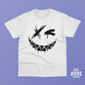May include: White t-shirt featuring a black graphic of a stylized, jagged-edged smile with an X for an eye and a tear-shaped element. The shirt has a crew neck and short sleeves. The KICKS CRAFT STUDIO logo is in the bottom right corner.