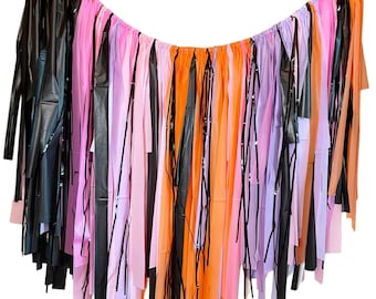 May include: A Halloween party decoration made of black, orange, pink, and purple tissue paper streamers. The streamers are tied together and hang in a curved shape.