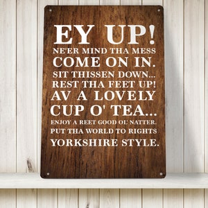 Peut inclure: Une plaque en métal brun rustique avec du texte blanc qui dit "Ey Up! Ne'er mind tha mess come on in. Sit thissen down... Rest tha feet up! Av a lovely cup o' tea... Enjoy a reet good ol' natter. Put tha world to rights Yorkshire style."