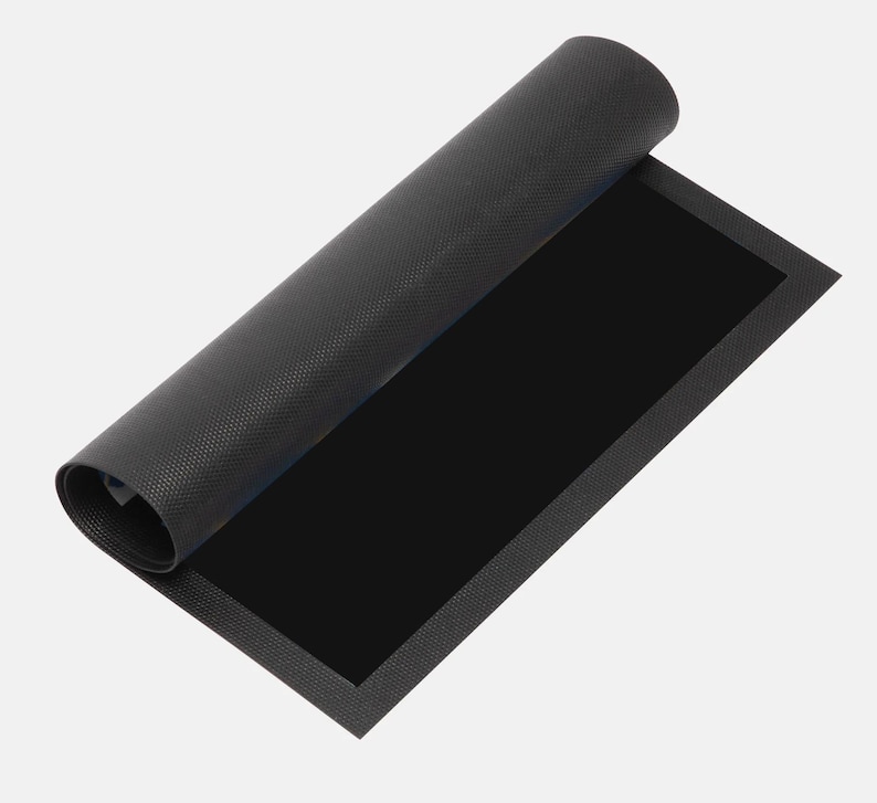May include: A rolled-up black mat with a textured surface. The mat is partially unrolled, revealing a solid black rectangular area. The edges of the mat have a slightly raised border.