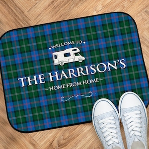 Peut inclure: Un paillasson de bienvenue en tartan bleu et vert avec le texte "Bienvenue chez les Harrison - Home from Home" et une silhouette blanche d'un camping-car.