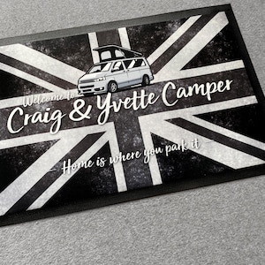 Może przedstawiać: Czarno-biała wycieraczka z motywem Union Jack i ilustracją kampera. Tekst brzmi "Welcome to Craig & Yvette Camper" i "Home is where you park it."