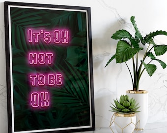 May include: A framed print with the text "IT'S OK NOT TO BE OK" in pink neon against a background of green tropical leaves. The print is in a black frame and is displayed with two white vases with plants.