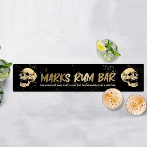 May include: Black bar runner with gold text that reads "MARKS RUM BAR" and "THE HANGOVER ONLY LASTS A DAY BUT THE MEMORIES LAST A LIFETIME". Two gold skull illustrations are on either side of the text.