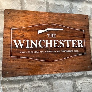 Peut inclure: Panneau en bois rectangulaire avec l'inscription blanche "THE WINCHESTER" et un dessin de fusil blanc. Le panneau comporte également la phrase "HAVE A NICE COLD PINT & WAIT FOR ALL THIS TO BLOW OVER." Le panneau a une finition en bois brun foncé.