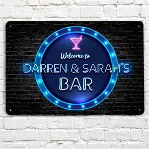 May include: A black metal sign with a neon blue circle and a pink martini glass. The sign says "Welcome to Darren & Sarah's Bar".