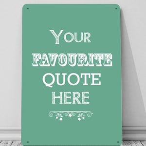 Puede incluir: Un letrero de metal verde azulado con texto blanco que dice "Your Favourite Quote Here". El texto está en un estilo de fuente vintage con un adorno decorativo en la parte inferior.
