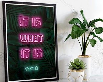 Op de afbeelding: Een ingelijst afdruk met een tropische bladeren achtergrond en neon roze tekst die "It is what it is" luidt met drie sterren onder de tekst.