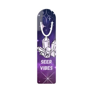 May include: A bookmark with a celestial design. The top features a white hook and stars against a dark blue background. Below, geometric crystals are set against a purple galaxy. The words "SEER VIBES" are printed at the bottom.