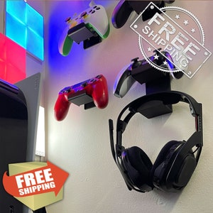 May include: A white wall with black wall mounts holding a black headset, a red and black video game controller, a green and white video game controller, and a white and black video game controller. The wall mounts are labeled "FREE SHIPPING".