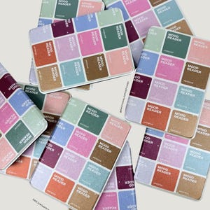Puede incluir: Una colecci&oacute;n de fundas para tel&eacute;fonos con un dise&ntilde;o de lector de estado de &aacute;nimo colorido. Cada funda presenta una cuadr&iacute;cula de cuadrados en varios colores, cada uno etiquetado con "MOOD READER" y un c&oacute;digo de color hexadecimal. Las fundas est&aacute;n dispersas sobre un fondo claro.