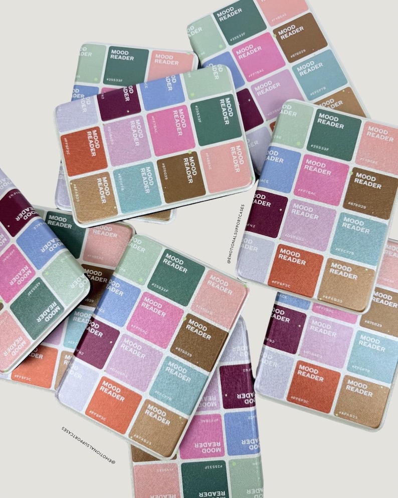 Puede incluir: Una colecci&oacute;n de fundas para tel&eacute;fonos con un dise&ntilde;o de lector de estado de &aacute;nimo colorido. Cada funda presenta una cuadr&iacute;cula de cuadrados en varios colores, cada uno etiquetado con "MOOD READER" y un c&oacute;digo de color hexadecimal. Las fundas est&aacute;n dispersas sobre un fondo claro.
