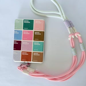 May include: A rectangular card featuring a grid of twelve color swatches, each labeled "MOOD READER" with a hex code. The card is attached to a long, multi-colored cord lanyard with white, lavender, and pink sections, featuring knotted details.