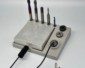 May include: A gray 3D printed tool holder with a metal plate and slots for holding various tools. The holder has a black cord attached to it and two screws are lying on the surface next to it.