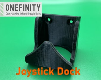 May include: A black 3D printed wall mount for a joystick, with the text "Joystick Dock" printed below. The mount has two holes for mounting screws.