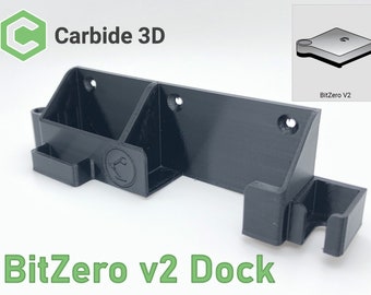 May include: A black plastic wall mount dock for the BitZero v2 3D printer. The dock has a slot for the printer and a hook for the power cord. The dock is labeled "BitZero v2 Dock" and has the Carbide 3D logo.