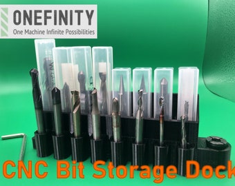 May include: A black CNC bit storage dock with 12 clear plastic containers holding various router bits. The dock has a black handle and a metal screw. The text "CNC Bit Storage Dock" is printed in orange below the dock.