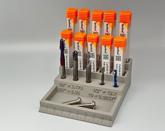 May include: A white plastic organizer with a ruler on the bottom and slots for holding 10 small orange and white tubes. The tubes contain small metal drill bits. The text on the organizer reads "1/8" = 3.175", "1/4" = 6.35", "1/2" = 12.7", and "10 = 0.3937".