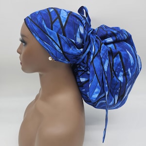 May include: A blue head wrap with a geometric pattern of black lines and shades of blue. The head wrap is tied in a bun at the back, with long ties hanging down. The fabric is wrapped around a mannequin head.