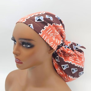May include: A brown and orange patterned surgical cap with blue and white geometric designs. The cap is tied at the back of the head.