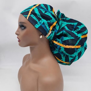 May include: A patterned head wrap in shades of teal, navy, and yellow. The fabric features a geometric design. The head wrap is tied in a bun at the back. The head wrap is displayed on a mannequin.