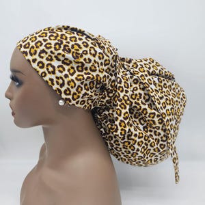 May include: A leopard print bonnet in shades of brown, black, and yellow. The bonnet is tied in a knot at the back, and is designed to protect the hair. The bonnet is made of a soft, silky material.