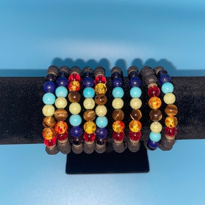 May include: A set of eight colorful beaded bracelets with lava rock beads. The bracelets feature a variety of colors, including red, orange, yellow, green, blue, and purple.