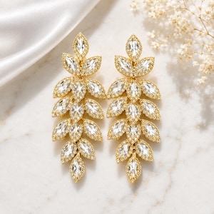 May include: A pair of gold-toned drop earrings featuring a leaf-inspired design. Each earring is composed of multiple marquise-cut clear crystals arranged in a cascading branch pattern, with each crystal bordered by tiny pavé-set stones.
