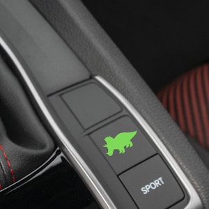 May include: A close-up of a car's interior with a green dinosaur-shaped button labelled "SPORT".