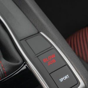 May include: Close-up of a car's interior featuring a black console with a silver trim. The console has two buttons, one labeled "BLOW JOB" in red and another labeled "SPORT" in white. Red stitching is visible on the black leather.