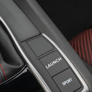 May include: Close-up of a black car interior with two buttons labeled "LAUNCH" and "SPORT".