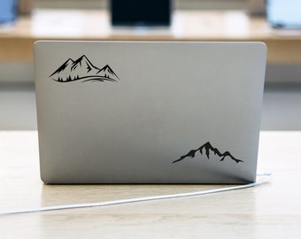 May include: A silver laptop with two black mountain range silhouette stickers on the back.