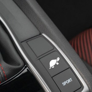 May include: A black car interior with a button that has a turtle icon and the word "SPORT" on it.