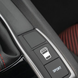 May include: A close-up of a car's interior with a black button with a white coffee cup icon and the word "SPORT" on a black button.