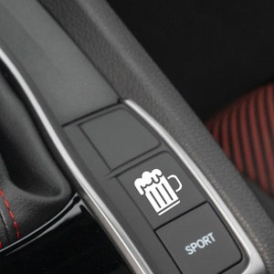 May include: A close-up of a car's interior with two buttons. The left button has a white icon of a beer mug. The right button is black and says "SPORT" in white letters.