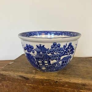 Può includere: Una ciotola per mescolare in ceramica blu e bianca con un motivo tradizionale di salice. La ciotola è appoggiata su una superficie di legno.