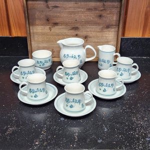 May include: A set of white ceramic teacups and saucers with a blue floral design. The set includes a creamer and sugar bowl.
