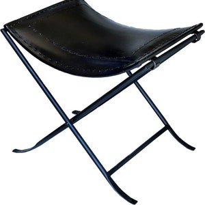 Puede incluir: Un taburete plegable de cuero negro con estructura de metal negro. El taburete tiene un asiento curvo y un diseño simple y minimalista.