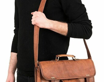 Puede incluir: Un maletín de cuero marrón con un bolsillo frontal y dos hebillas a cada lado. La bolsa tiene un asa superior y una correa de hombro larga ajustable.