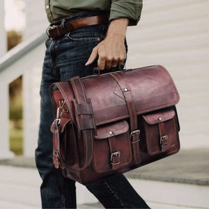 Puede incluir: Un maletín de cuero marrón con múltiples bolsillos y hebillas. La bolsa tiene un asa superior y una correa para el hombro.