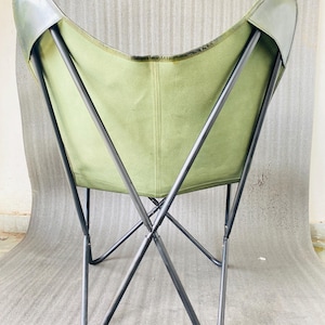 May include: A green canvas butterfly chair with a black metal frame. The chair is folded and the back is facing the camera.