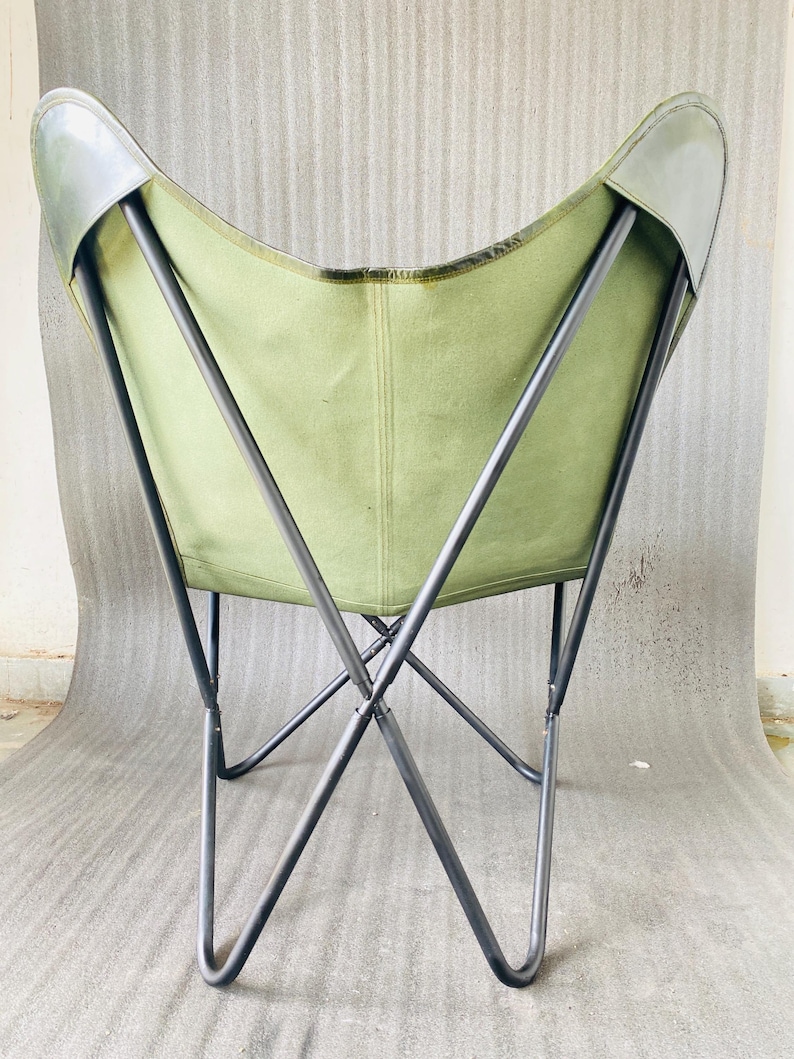 May include: A green canvas butterfly chair with a black metal frame. The chair is folded and the back is facing the camera.