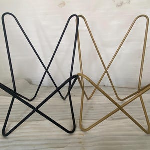 May include: Two butterfly chairs, one black and one gold, are shown on a white surface. The chairs are made of metal and have a simple, modern design.