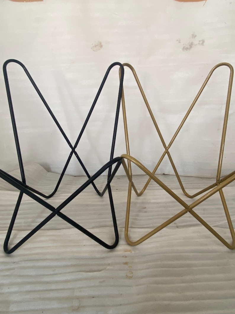 May include: Two butterfly chairs, one black and one gold, are shown on a white surface. The chairs are made of metal and have a simple, modern design.