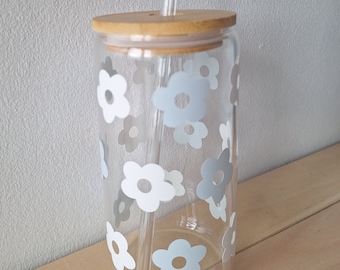 May include: A clear glass tumbler with a bamboo lid and a straw. The tumbler has a floral pattern with white and light blue flowers.